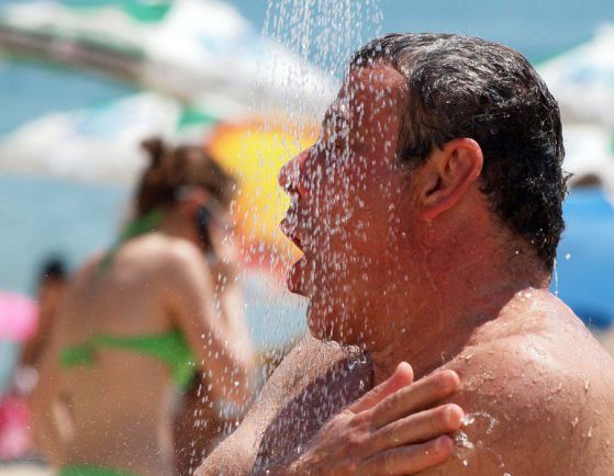Мъж се разхлажда под душ на плажа в горещото време. Снимка: БГНЕС