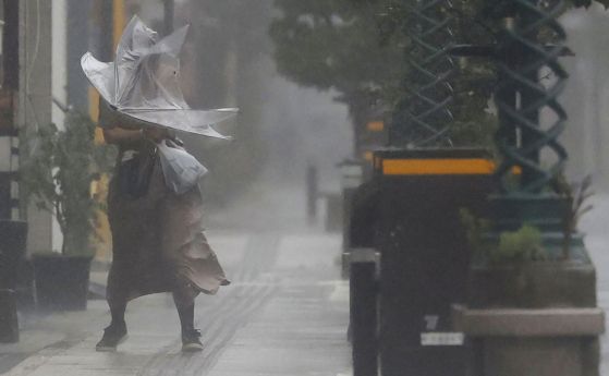 Жена си проправя път през силния вятър и дъжда в Миязаки, Южна Япония, неделя, 18 септември 2022 г., когато мощен тайфун връхлетя Южна Япония.