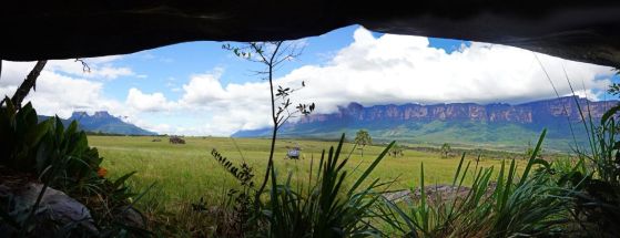 Панорамна гледка от вътрешността на пещерата на тревиста равнина със скалисти хълмове