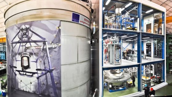 Съоръжението XENON1T, вляво е резервоарът за вода, съдържащ самия инструмент, с плакат, показващ какво има вътре – вдясно е триетажната сервизна сграда.