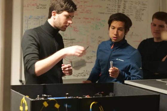 Тобиас Бауер (вляво) и Марлон Шефер (вдясно) от университета в Саарланд и Тим Щробел (в центъра) от университета в Щутгарт се подготвят за експеримент с мобилни квантови честотни преобразуватели