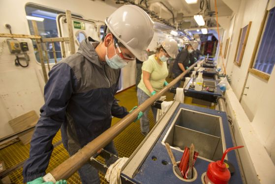 Горе вляво, Оскар Кавасос (специалист по морска лаборатория, IODP JRSO) се присъединява към други морски специалисти в подготовката на ново седиментно ядро, което ще бъде секционирано на подиума на JOIDES Resolution през 2022 г.