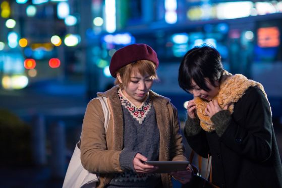 2 young women using a tablet computer at night