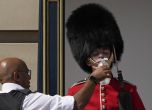 Полицай дава вода на британски войник, носещ традиционна шапка от меча кожа, който е на пост пред Бъкингамския дворец в горещото време в Лондон, понеделник, 18 юли 2022 г. 