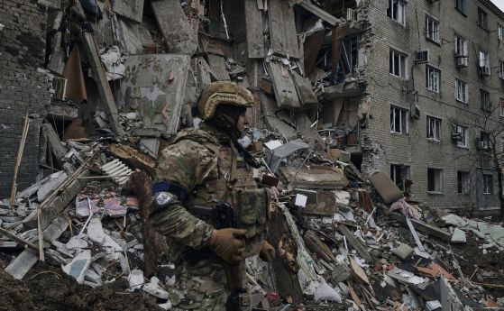 Украински войник пред разрушена жилищна сграда.