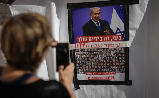 Жена снима плакат със снимки на заложниците в Газа под изображението на министър-председателя Бенямин Нетаняху, който призовава останалите израелски водачи да постигнат споразумение за връщането им у дома. Тел Авив, 21 ноември 2023 г.