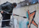Човек чисти графитите на НДК със специална пароструйка и маска