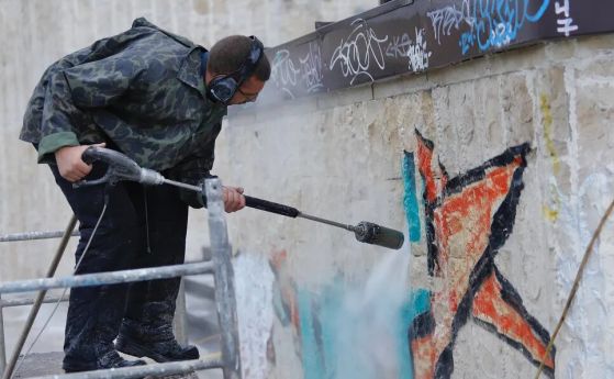 Човек чисти графитите на НДК със специална пароструйка и маска