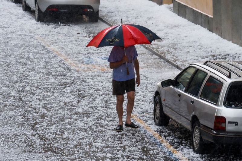 Мъж с чадър на улица, покрита с късове градушка