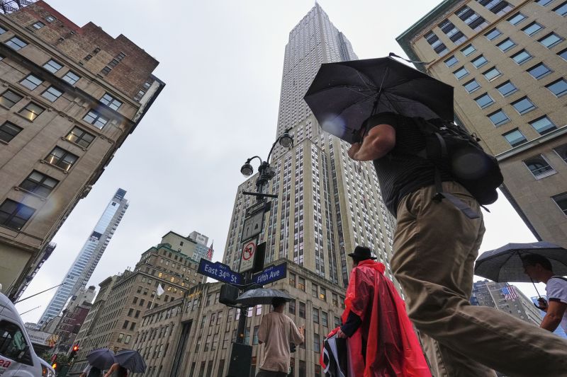 Пешеходци с чадъри и дъждобрани преминават вчера покрай небостъргача 